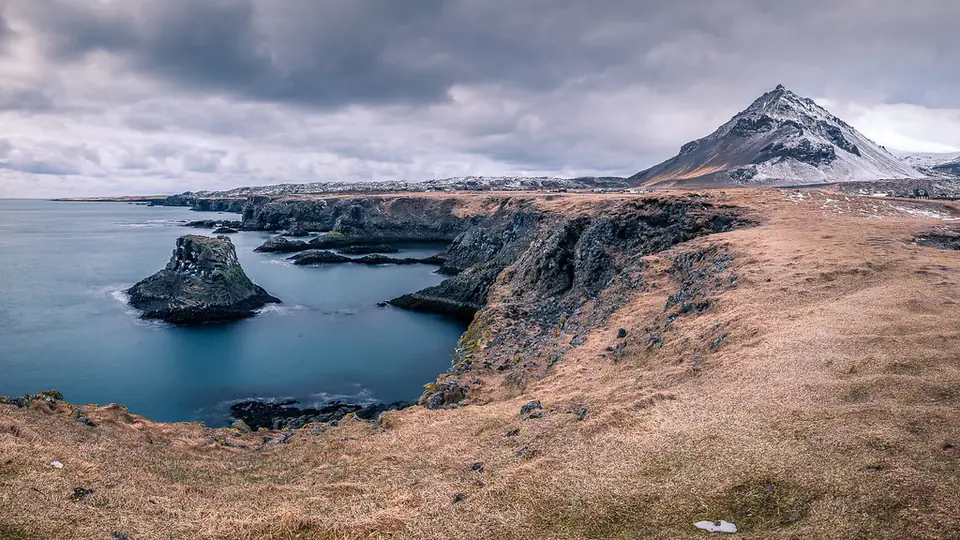 Kusten vid Arnarstapi med klippor i vattnet och Snæfellsjökull i bakgrunden