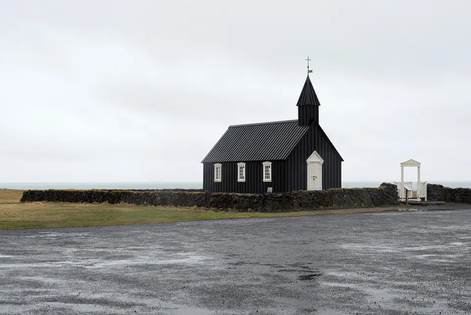 Búðakirkja mit Friedhofstor und Steinmauer an einem grauen Tag
