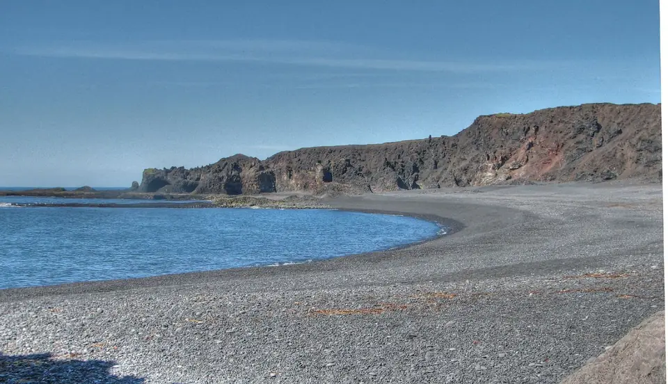 Bucht Dritvík mit Kiesstrand und Klippen bei blauem Himmel