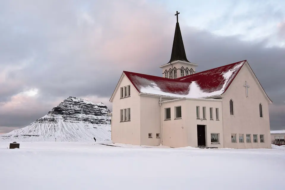 Weiße Kirche von Grundarfjörður mit rotem Dach im Schnee, dahinter der Kirkjufell