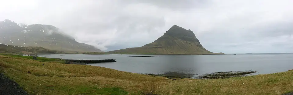 Kirkjufell vom Ufer des Grundarfjörður aus gesehen, mit Wasser und Wiesen im Vordergrund