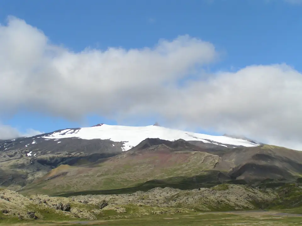 Snæfellsjökull mit Schneefeldern über grünem Hang unter Wolken